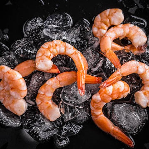 Cooked jumbo cocktail shrimp, tail-on, arranged on ice against a black background — ready to serve with dipping sauce or lemon wedges.