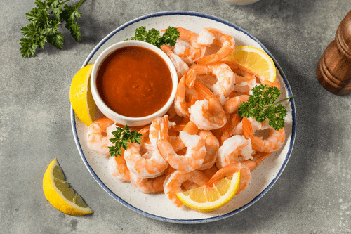 Wild-caught Key West Pink Shrimp, 10/20 count, served on a plate with lemon wedges, cocktail sauce, and a pepper shaker — premium seafood presentation.
