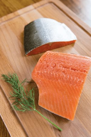 Two pieces of wild Alaskan sockeye salmon 6 oz fillet on a wooden cutting board with a sprig of greens.